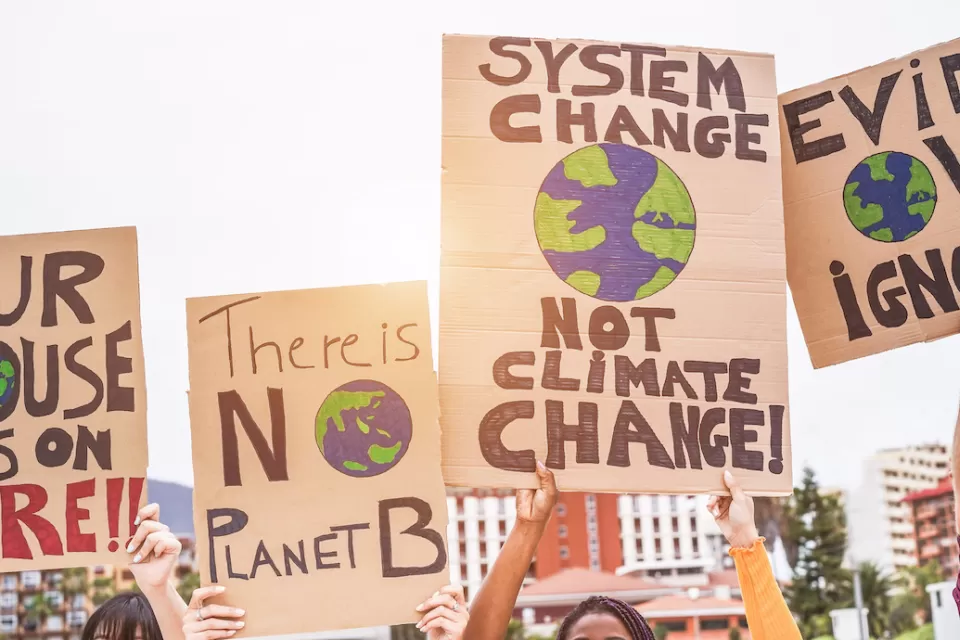 Close-up of signs calling for action on climate change being help up by multiple people outdoors.